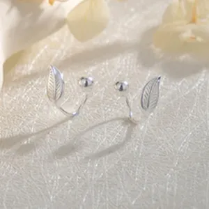 Delicados pendientes de botón con hoja y cuenta plateada, elegante primer plano de joyería.