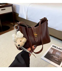 Brown leather shoulder bag with cute bear charm, elegant commuter hobo bag detail shot.