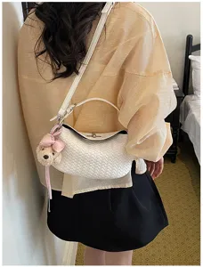 Detail view of stylish white woven shoulder bag featuring a cute bow bear charm.