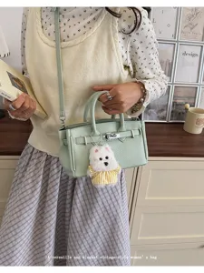 Detail view of stylish mint green leather Kelly bag with cute plush dog charm pendant.