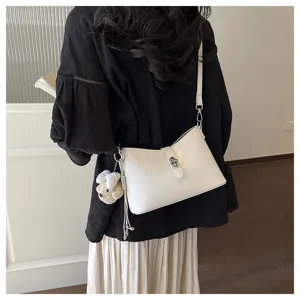 Detail shot of a minimalist white underarm shoulder bag with metal lock and cute plush charm.