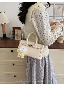 Close-up detail of stylish beige lychee pattern handbag with cute plush dog pendant.