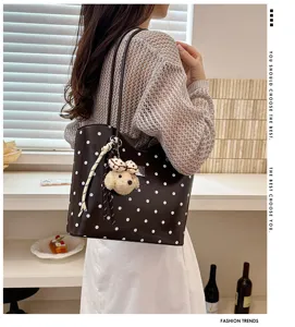 Detail shot of stylish polka dot tote bag with cute bear pendant, worn on shoulder in modern room.
