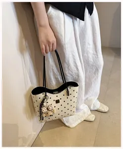 Close-up of stylish polka dot shoulder tote bag featuring cute bear pendant and handles.