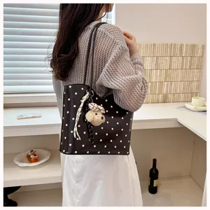 Detail shot of women's polka dot leather tote bag featuring a cute plush bear pendant and ribbon.