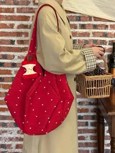 Vista detallada de un bolso de lona rojo con estampado floral y un lindo colgante de manzana.
