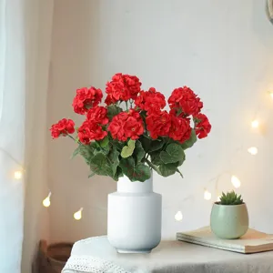 Detailed close-up of vibrant red artificial geranium bouquet in white ceramic vase for decor.