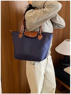 Women nylon tote bag detail, featuring classic dumpling shape with brown leather handles.