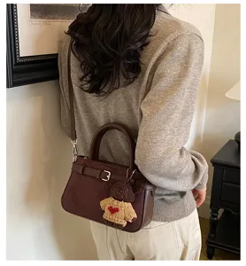 Close-up view of a retro brushed shoulder bag with cute bear pendant and metal buckle.