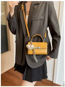 Detail view of a vintage yellow small square handbag with metal lock and heart knit pendant.