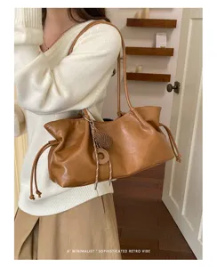 Detail shot of slouchy brown retro tote bag with shoulder strap and stylish woven charm accent.