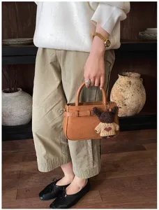 Vintage brown suede top handle handbag with cute knit bear pendant for daily commuting.