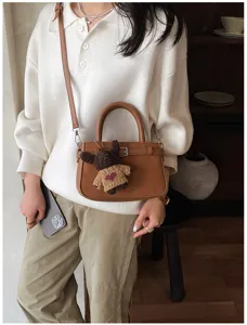 Detail view of the brown suede handbag with a cute bear pendant, showing daily commuter style.