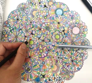Detailed view of colored pencil in action, coloring intricate floral mandala pattern page.