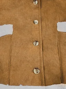 Ribfluwelen gilet detail met bruine textuur, knopen en witte pluche zakafwerking voor dames.