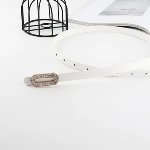 Gros plan détaillé d'une fine ceinture en cuir blanc pour femme avec boucle carrée en strass.