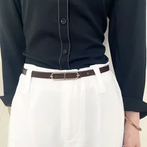 Detail shot of a minimalist thin brown leather belt with elegant gold buckle worn by model.