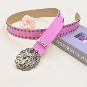 Dettaglio cintura in pelle rosa con borchie, fibbia a farfalla strass e rosa decorativa.