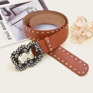 Close-up of wide brown studded belt featuring sparkling rhinestone ornate buckle detail.