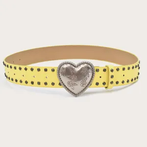 Close-up detail of the yellow leather belt featuring double-row metal studs and heart buckle.