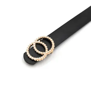 Close-up detail of the elegant black leather belt with gold pearl interlocking buckle.
