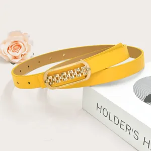 Yellow women's thin leather belt featuring gold rhinestone geometric buckle close-up.