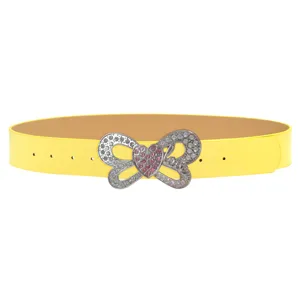 Detalle de cinturón de cuero amarillo con mariposa de pedrería brillante y hebilla rosa.