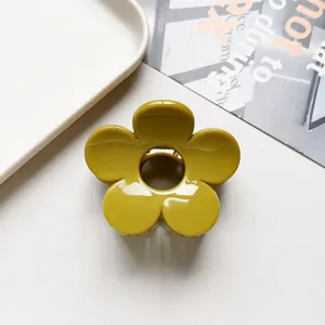 Close up detail of the glossy mustard yellow flower hair claw clip on white background surface.