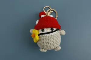 Primo piano di un portachiavi a pinguino all'uncinetto con cappello a fungo rosso.
