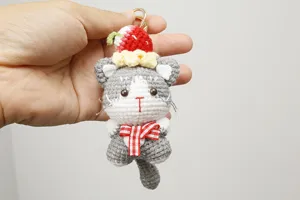 Porte-clés chat gris au crochet fait main avec pendentif gâteau fraise et détail sac.