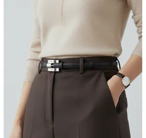 Detailed view of a slim black leather belt with a sophisticated silver metal buckle on a model.