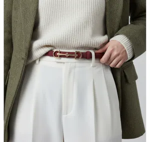 Detail shot of a stylish burgundy thin leather belt with a luxury gold horsebit buckle.