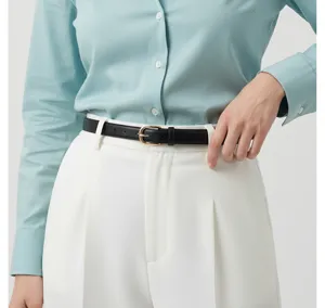 Detail view of slim black leather belt with gold buckle worn on white trousers for women.