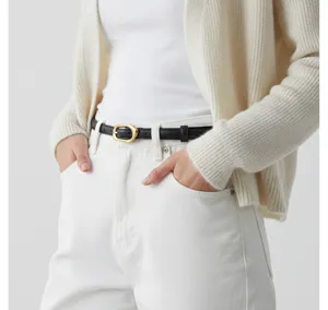 Close-up detail of the sleek black leather belt with gold irregular buckle worn on white jeans.