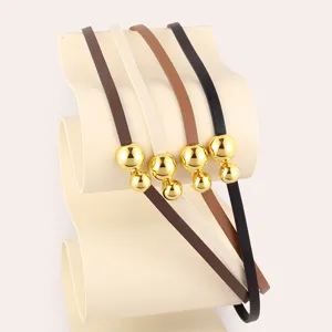Close-up detail of stylish thin leather belt featuring shiny gold spherical metal buckles.