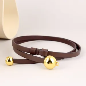 Details of the brown leather thin waist belt featuring a shiny gold metal ball closure.