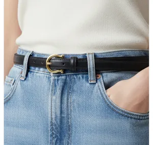 Close-up detail of a minimalist black leather belt with a polished gold horseshoe metal buckle.