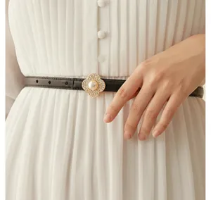 Detail shot of a slim black leather belt featuring an elegant pearl clover metal buckle.