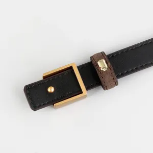 Close-up detail of slim black leather belt with square gold buckle and stylish keeper design.