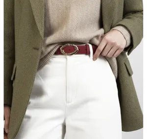 Close-up detail shot of a burgundy leather belt with irregular gold buckle worn on white pants.