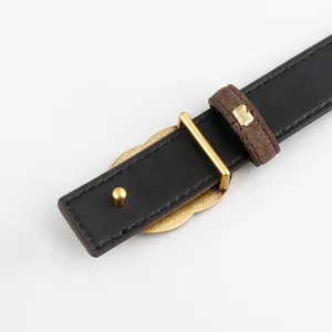 Gros plan d'une fine ceinture en cuir noir avec boucle dorée en trèfle et passant suède.
