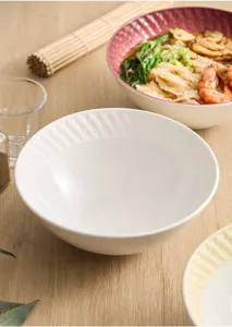 Detail view of white ceramic noodle bowl with geometric rim texture on wooden table.