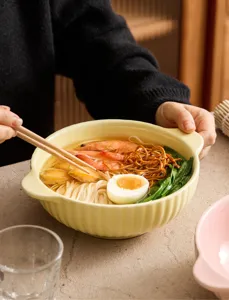 Detailed shot of a yellow ceramic noodle bowl with vertical stripes and double handles.