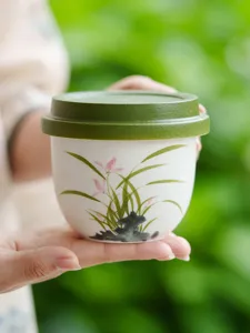 Handgefertigte Keramikteetasse mit grünem Deckel und feinem handbemalten Orchideendetail.