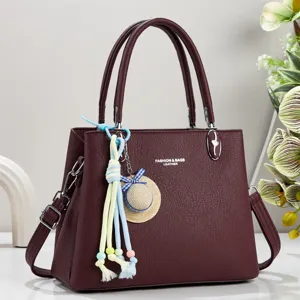 Detaillierte Nahaufnahme einer eleganten burgunderroten Ledertasche mit zwei Henkeln und Anhänger.