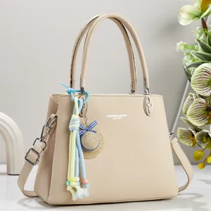 Detailansicht der eleganten beige Damentasche mit dekorativem Anhänger und hochwertigen Beschlägen.