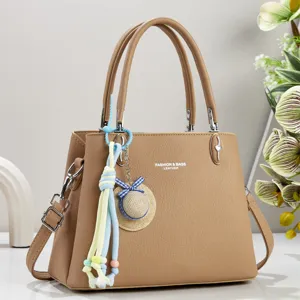 Nahaufnahme der khakifarbenen Ledertasche mit schickem Strohhut-Anhänger und Metallbeschlägen.
