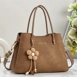 Detailed view of brown textured women handbag with elegant flower charm and metal hardware.