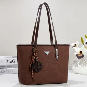 Λεπτομέρεια καφέ δερμάτινης τσάντας shopper, με διπλές λαβές ώμου και κομψό μενταγιόν.