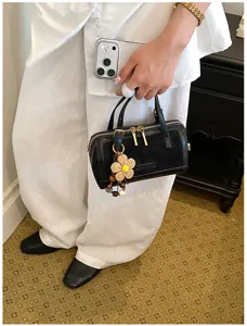 Close-up detail shot of a stylish black mini Boston handbag featuring a cute woven flower charm.